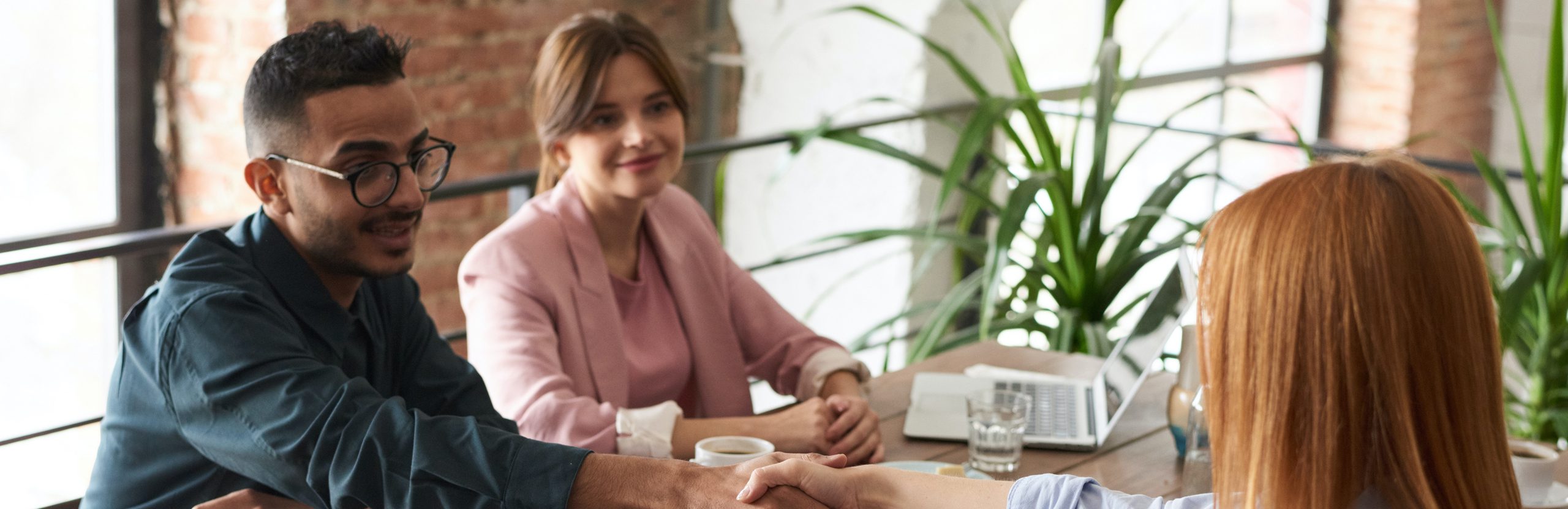 Graduate Admissions. A group of people sitting at the table. The two people in the foreground are shaking hands. A group of people sitting at the table. The two people in the foreground are shaking hands.