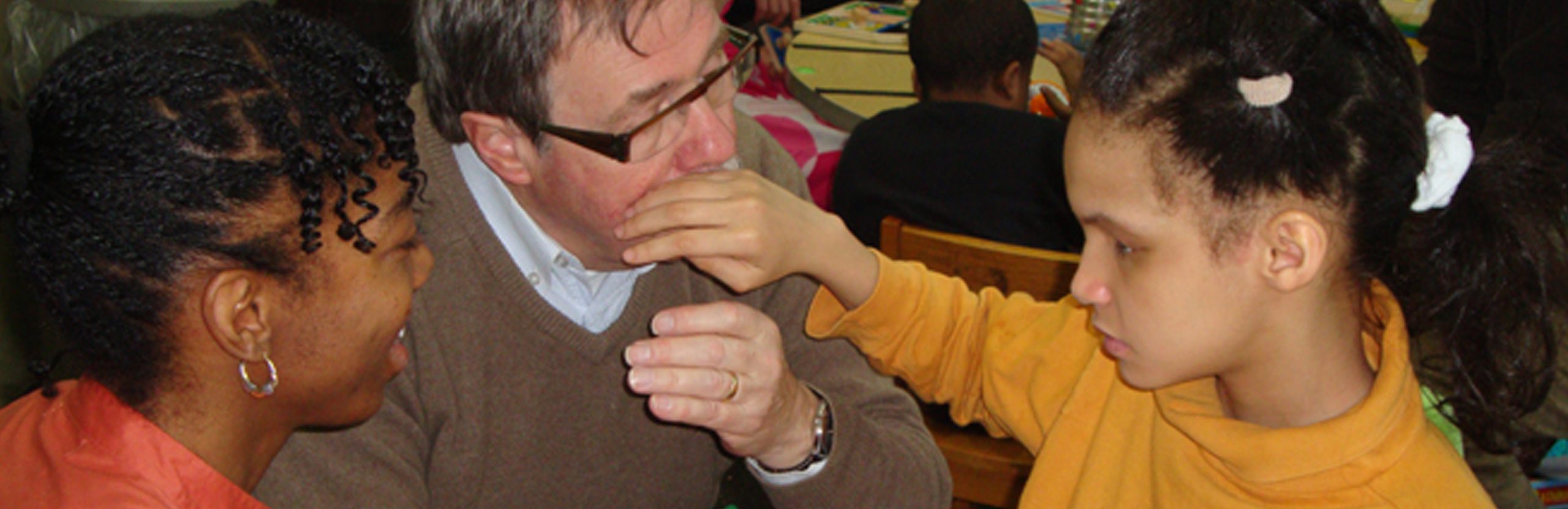 New York Deaf Blind Collaborative-A girl touches the face of the person next to her. Beside them a person is observing and smiling. A girl touches the face of the person next to her. Beside them a person is observing and smiling.